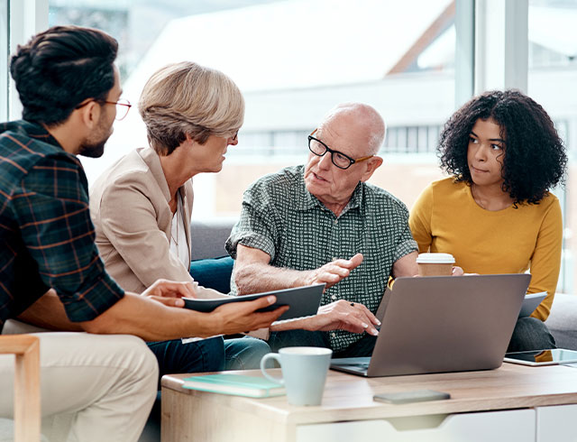 two men and two women sitting around a coffee table and laptop talking