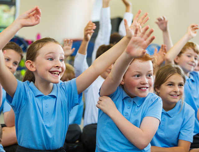 Young kids in uniforms excitedly raising their hands