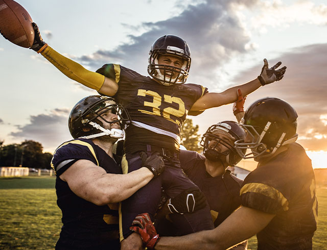 three high school football players celebrating by lifting up their friend
