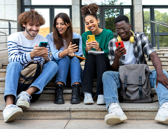 group of high school students sitting on steps looking at their phones and laughing