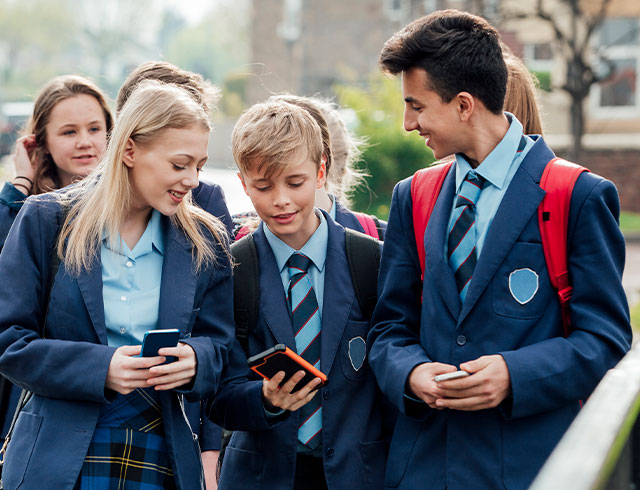 several students in uniforms looking at their phones